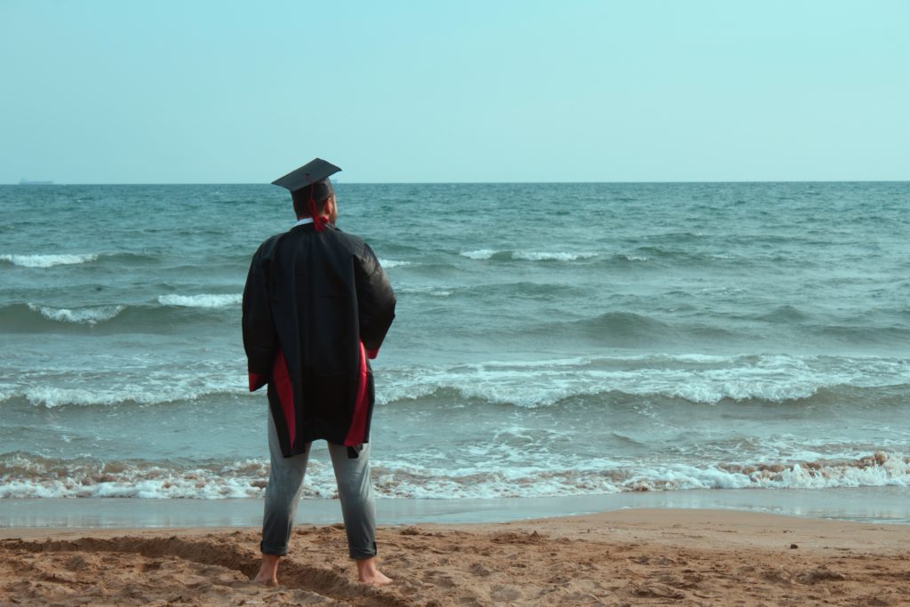 Man in graduation uniform standing by the sea